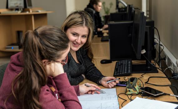 Two young girl students working at their desks in a university library.